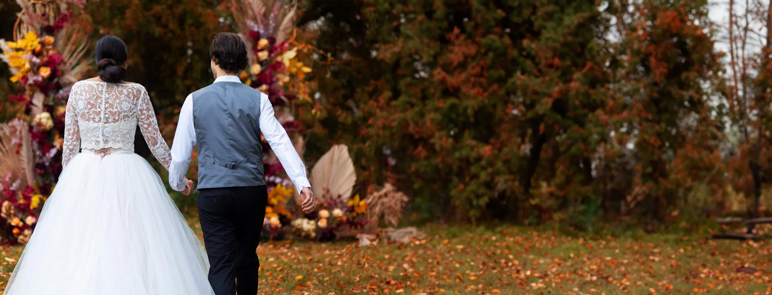 Bride and groom walking hand in hand through a fall foliage arch at a Thanksgiving weekend wedding