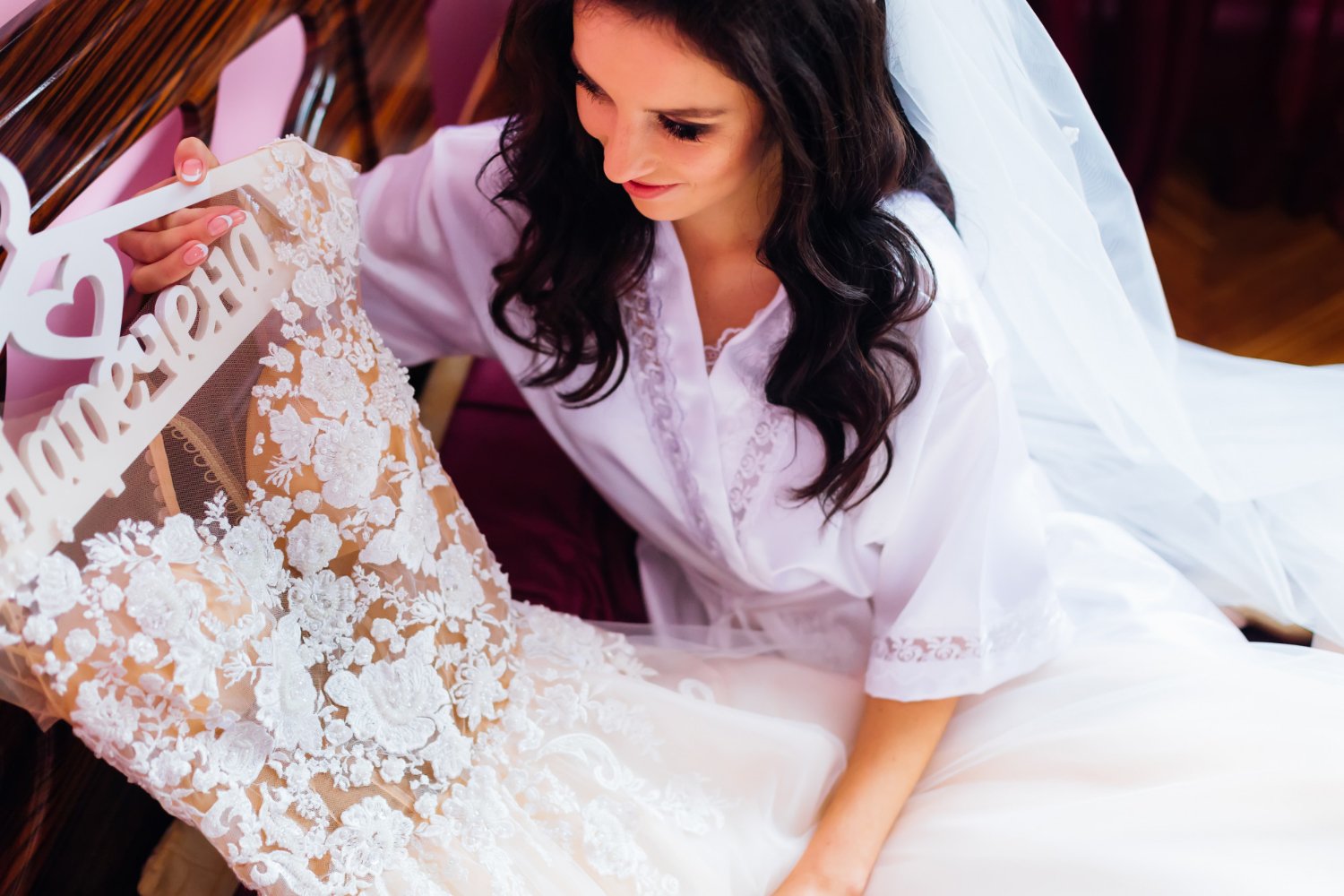 Wedding Dress Alterations: Hidden Costs and Fees the Quote May Not Show 19 Bride in bathrobe and bridal veil holds a hanger with a wedding