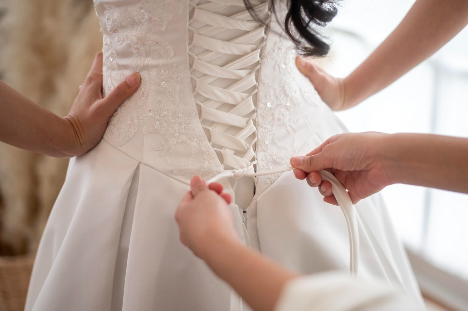 Wedding Dress Alterations: Hidden Costs and Fees the Quote May Not Show 17 Close up of tying bow on elegant white bridal wedding dress