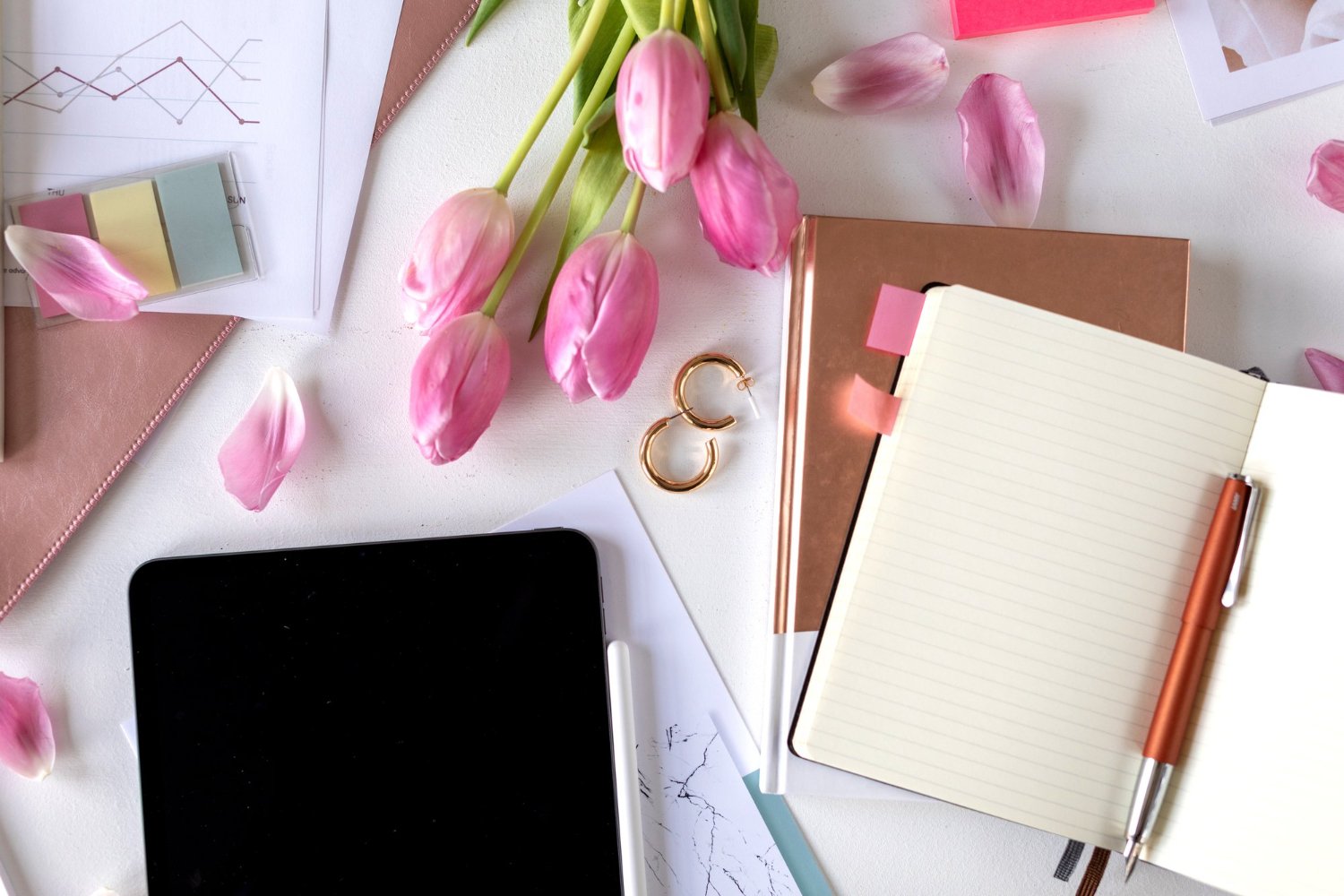 Second Photographer & Videographer Add-Ons: What They Actually Cost and Cover 13 Elegant workspace with a tablet, notebook, pen, and pink tulips for reviewing a photography contract