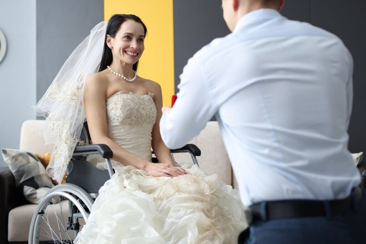 Groom placing a wedding ring on his bride's hand while she sits in her wheelchair at an accessible wedding venue