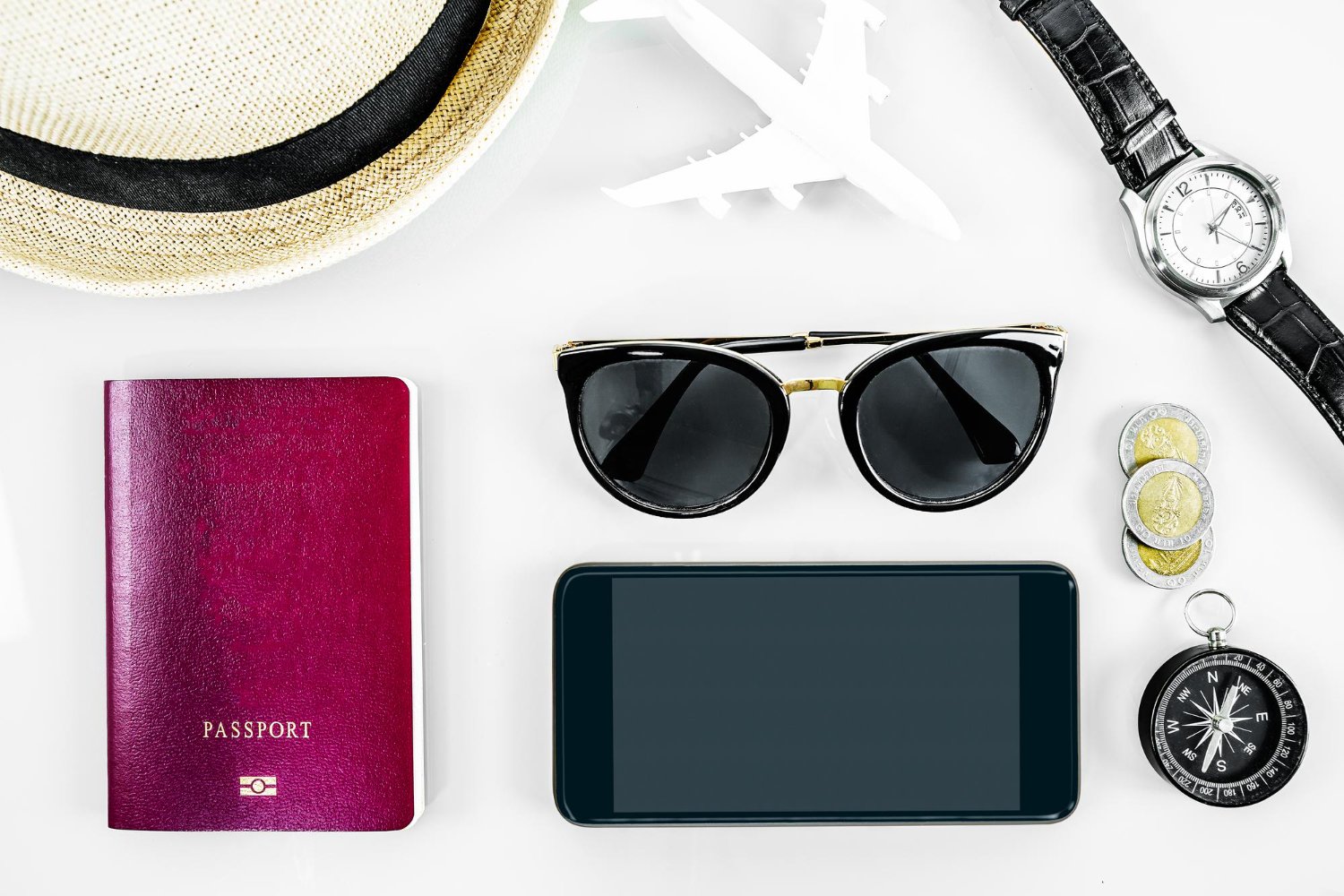 Honeymoon Travel Insurance Coverage: What Each Type of Policy Actually Pays For 11 Passport, sunglasses, and phone arranged on a clean white background for honeymoon travel insurance planning
