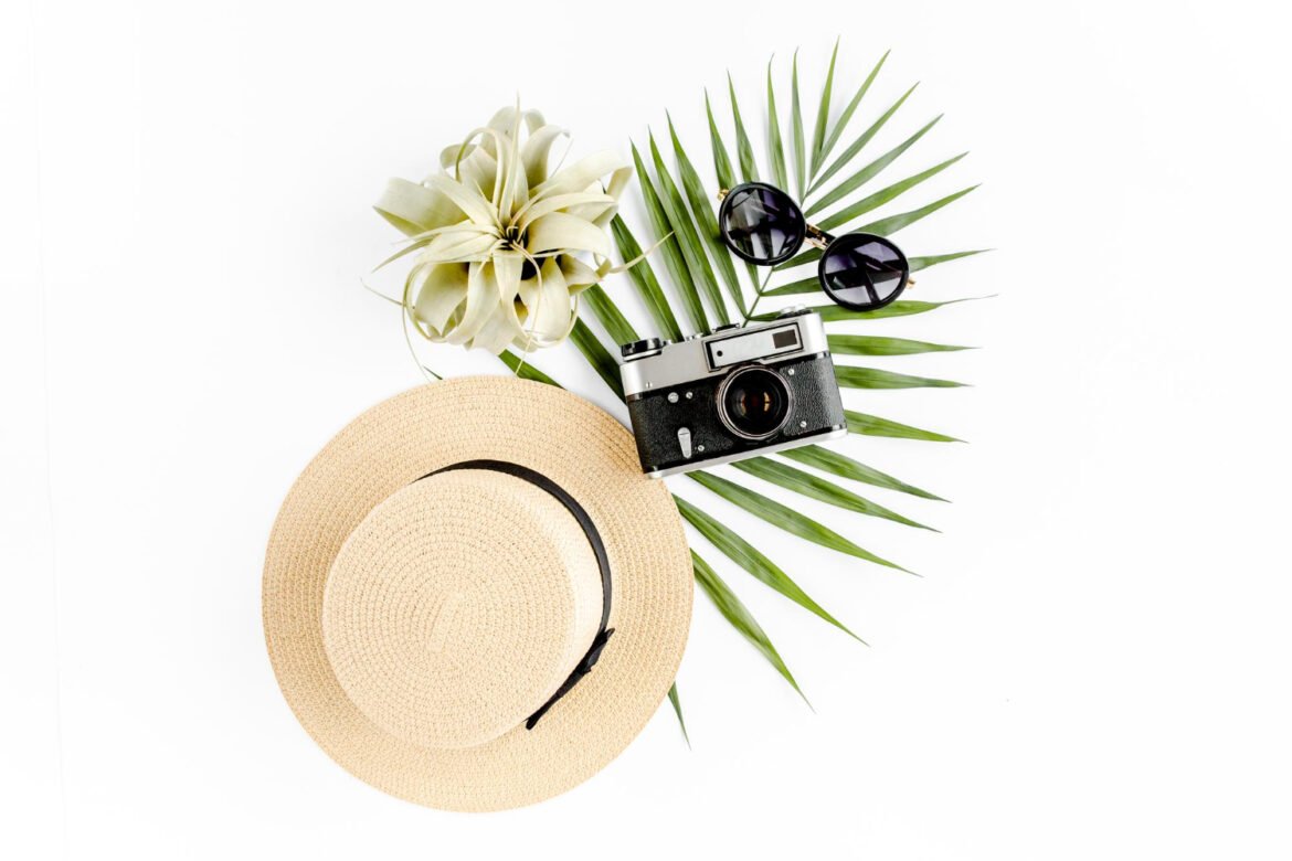 Elegant flat lay of travel essentials with a straw hat, retro camera, sunglasses, and palm leaf for a honeymoon trip