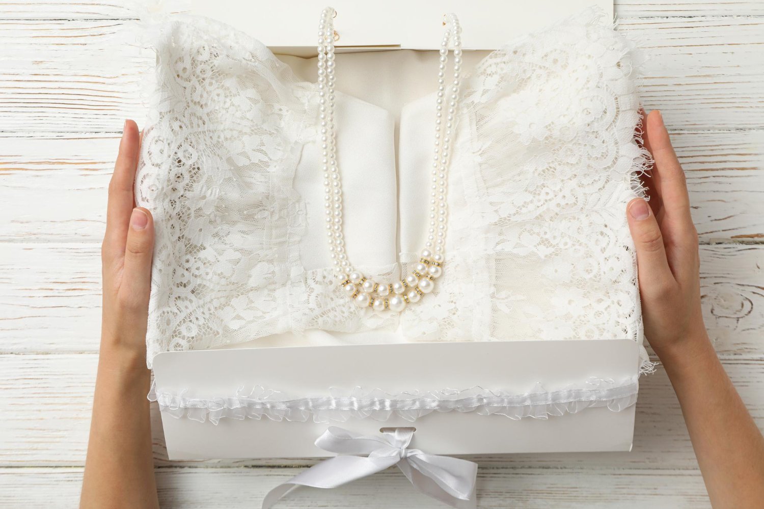 Bride's hands carefully placing a lace wedding dress into a preservation box with pearls