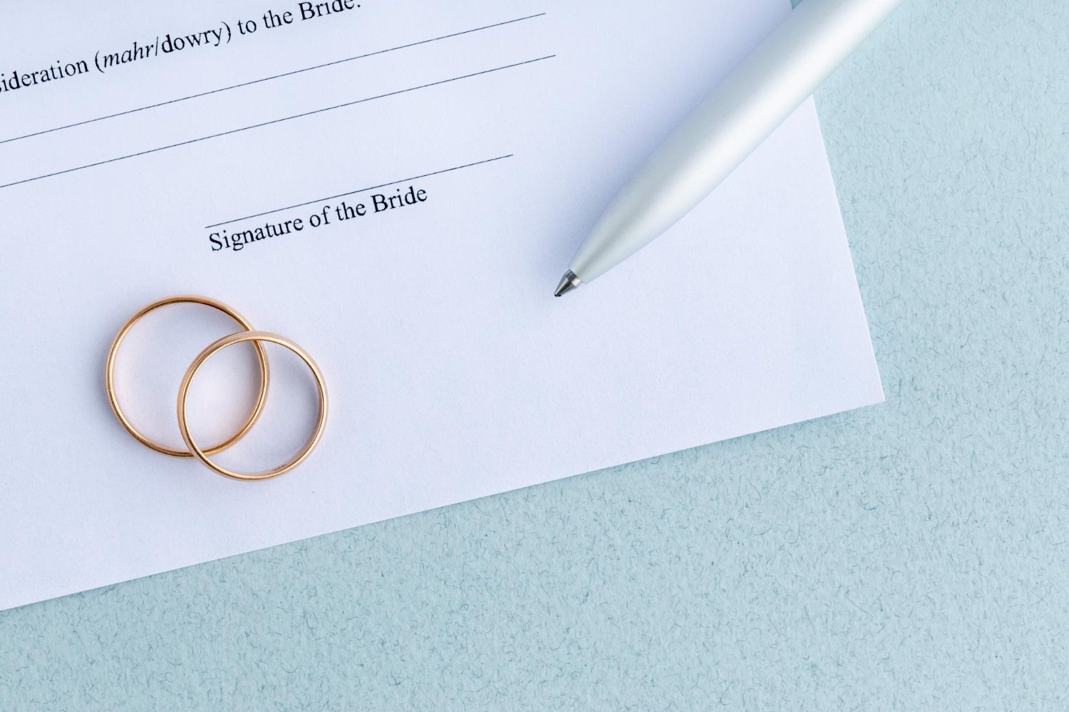 Name Change After Marriage: Costs, Deadlines, and the Paperwork Nobody Explains 12 Close-up of wedding rings resting on a marriage certificate signature line with a pen