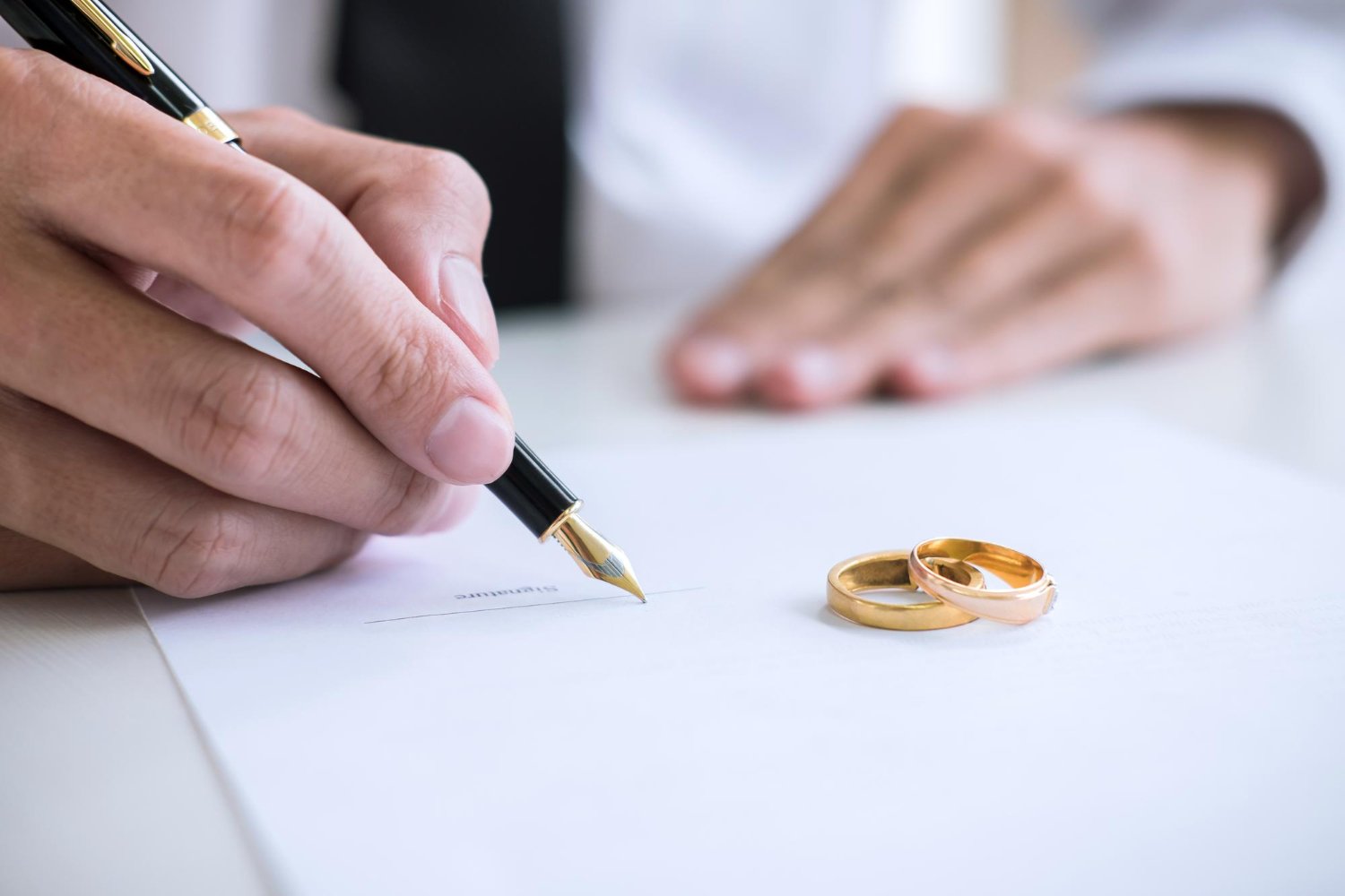 Wedding Officiant Cost: Hidden Fees and Questions to Ask Before You Book 9 Close-up of a hand signing a wedding contract next to gold wedding rings