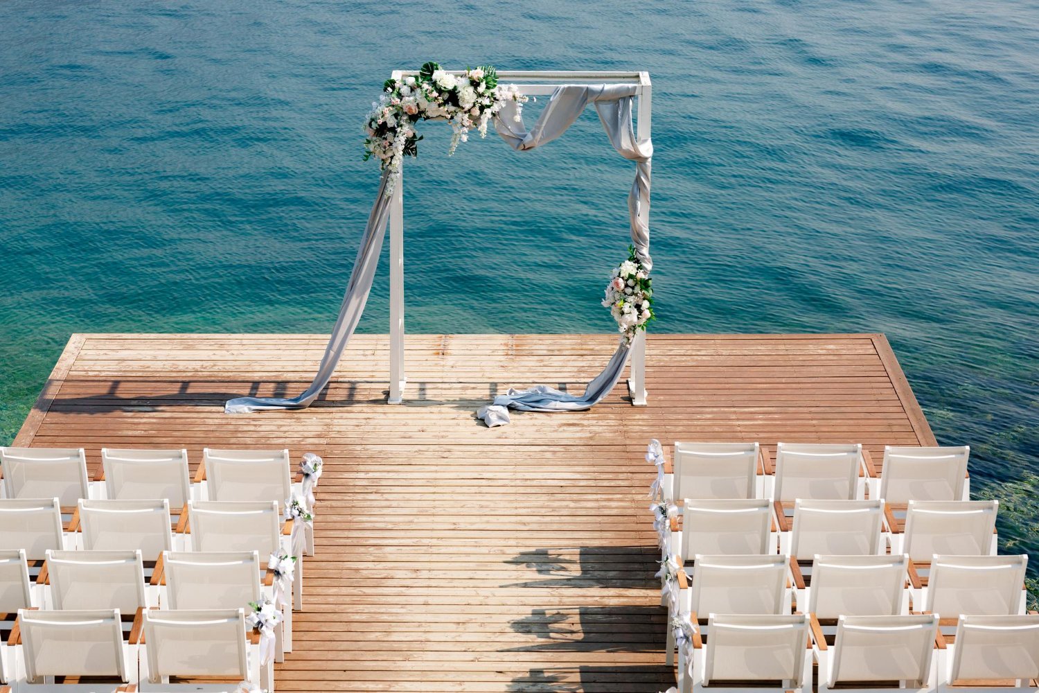 Destination Wedding Guest Costs: What to Really Expect (and How to Budget) 10 Elegant wedding arch on a wooden pier overlooking the ocean with rows of chairs